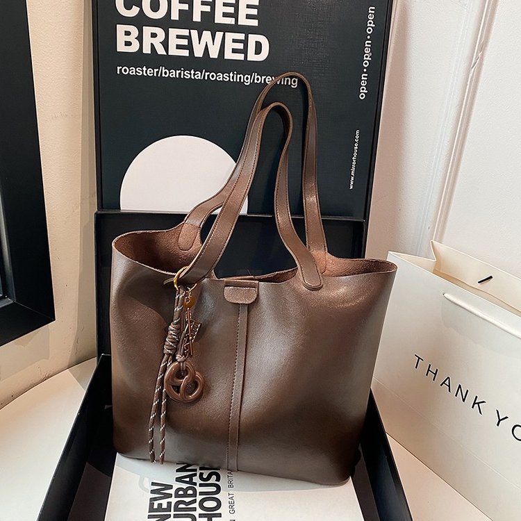Brown leather tote bag with decorative charm on a surface with a blurred background